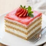 A spatula lifting a serving of soft strawberry eclair cake from a pan.