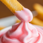 Close-up of a french fry being dipped into a thick strawberry frosty.