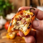 Close-up of a hand holding a bitten stuffed mini pepper showing the creamy filling.