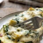 Close-up of a fork cutting into a creamy spinach and artichoke stuffed zucchini boat.