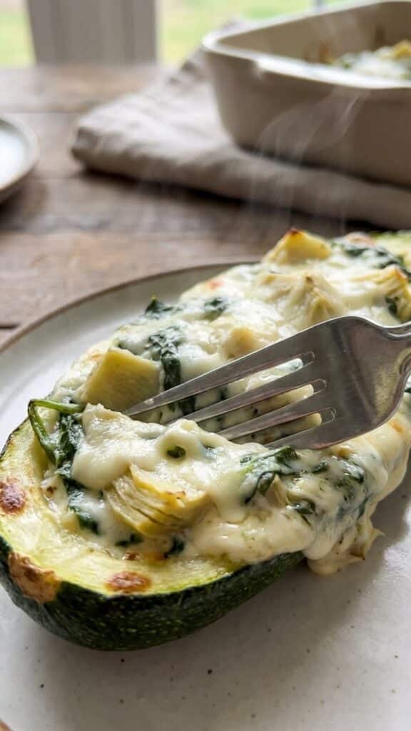 Close-up of a fork cutting into a creamy spinach and artichoke stuffed zucchini boat.