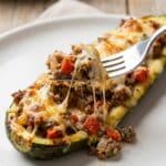 Close-up of a fork cutting into a cheesy stuffed zucchini boat showing the savory filling.