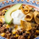 Close-up of a serving of taco casserole topped with sour cream and avocado.