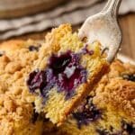 Close-up of a fork cutting into a piece of blueberry buckle showing a burst berry.