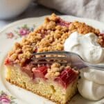 Close-up of a slice of rhubarb streusel cake served with a dollop of whipped cream.