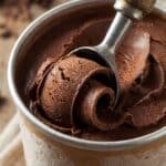 Close-up of a metal scoop curling through deep dark chocolate ice cream.