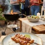 Honey chicken kabobs served over rice on a patio table with a grill in the background.