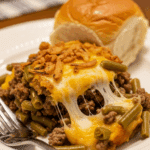 Plated serving of hamburger green bean casserole with a fork and a dinner roll.