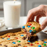 9x13 baking pan of cut M&M cookie bars with a hand taking a square.