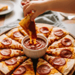 Hand dipping a crispy pepperoni quesadilla wedge into tomato sauce.