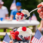 Hand holding a serving cup of patriotic cheesecake salad at a summer backyard party.