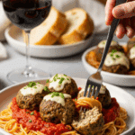 Plated spaghetti dinner with spinach mozzarella meatballs, red wine, and bread.
