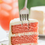 Slice of strawberry lemonade cake served on a plate with a glass of pink lemonade.