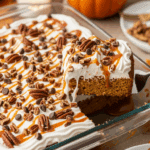 9x13 pan of finished Pumpkin Poke Cake topped with toffee and caramel, with a slice being served.