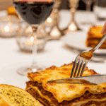 Plated slice of Million Dollar Lasagna with garlic bread and red wine.